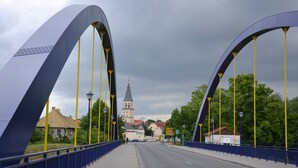 A bridge with large arches, a road, and a church in the background.