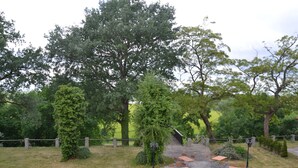 An outdoor seating area with tables and benches, surrounded by trees and a stone fence.
