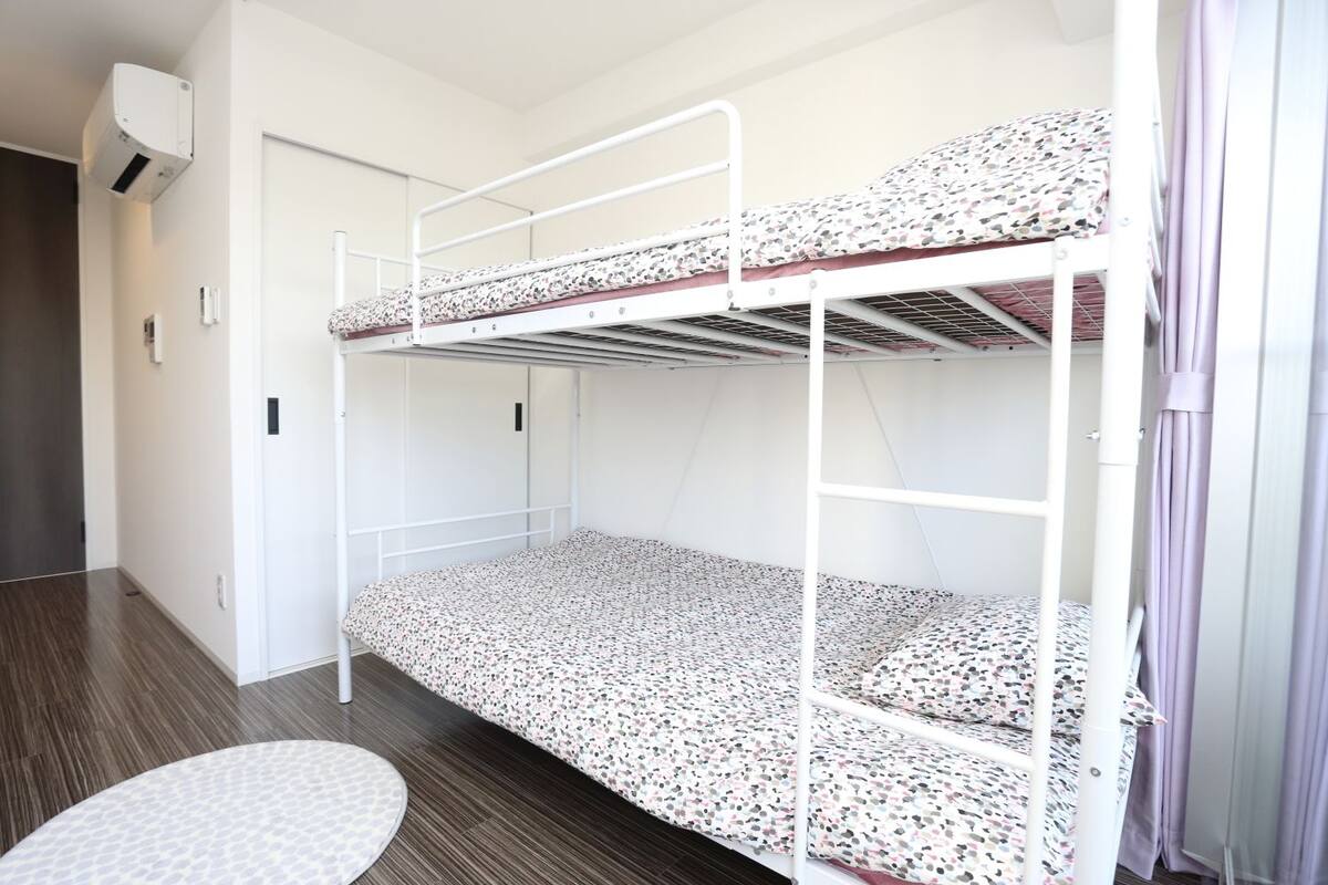 Une chambre avec un lit superposé, un matelas à motifs, un tapis rond et une porte blanche.