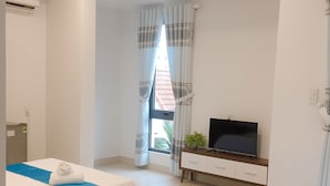 Habitación de hotel con dos camas, televisión, una planta pequeña y una ventana con cortinas.