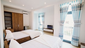 Habitación de hotel con dos camas, televisión, escritorio y balcón con cortinas.