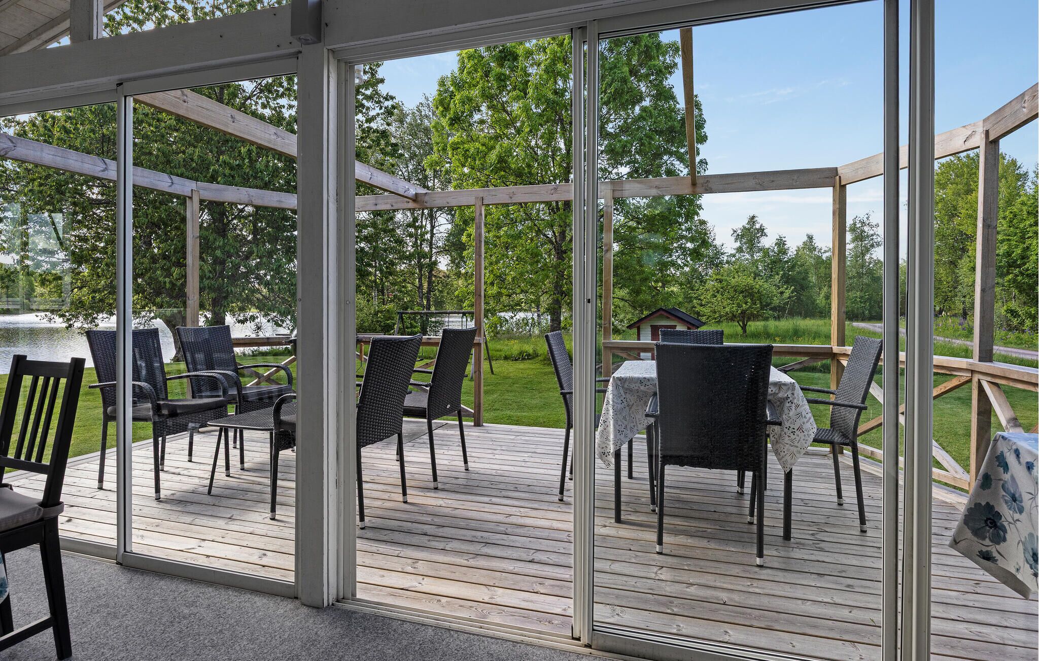 A covered outdoor deck with chairs and tables, surrounded by glass walls.