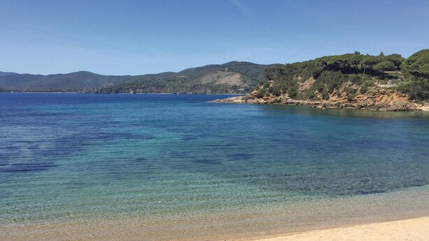 A beach with clear water, sandy shore, and hills in the background. - 2 bedroom amazing apartment in Porto Azzurro (Porto Azzurro)