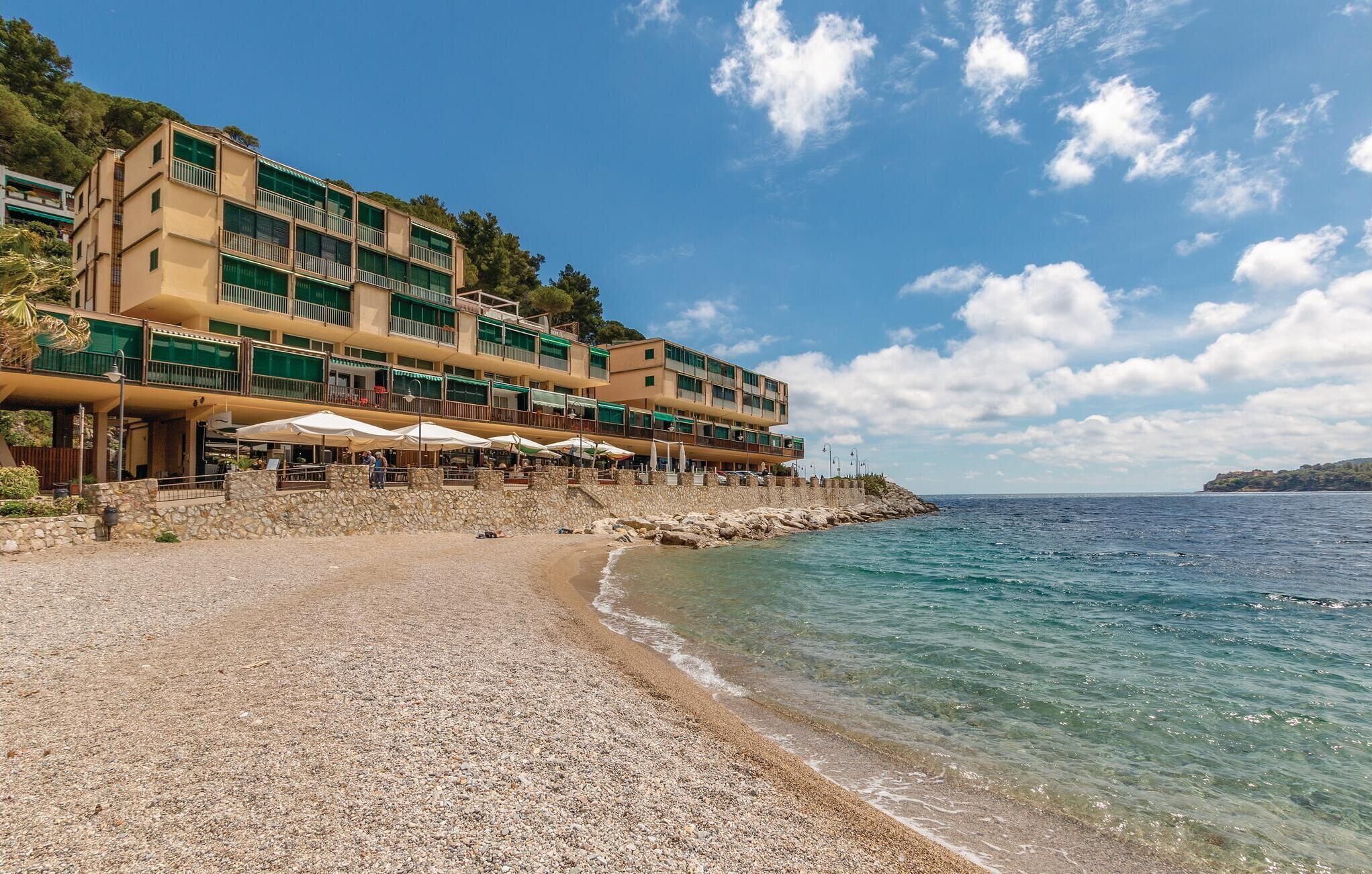 Um hotel à beira-mar com várias varandas, área de estar ao ar livre e uma praia de pedras.