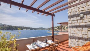 An outdoor dining area with a table set for two, overlooking a body of water and a coastal landscape. - 2 bedroom amazing apartment in Porto Azzurro (Porto Azzurro)