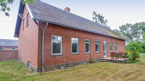 A red brick house with a sloped roof, multiple windows, and a small porch with outdoor furniture. - Nice home in Sakskøbing with WiFi (Sakskøbing)