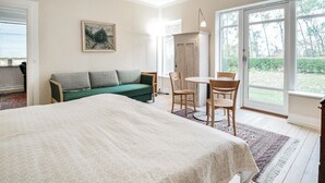 A bedroom with a large bed, a green sofa, a dining table with chairs, and a sliding glass door leading to a garden. - Nice home in Sakskøbing with WiFi (Sakskøbing)