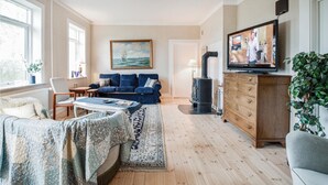A cozy living room with a blue sofa, a wooden cabinet, a television, and a painting of a sailboat. - Nice home in Sakskøbing with WiFi (Sakskøbing)
