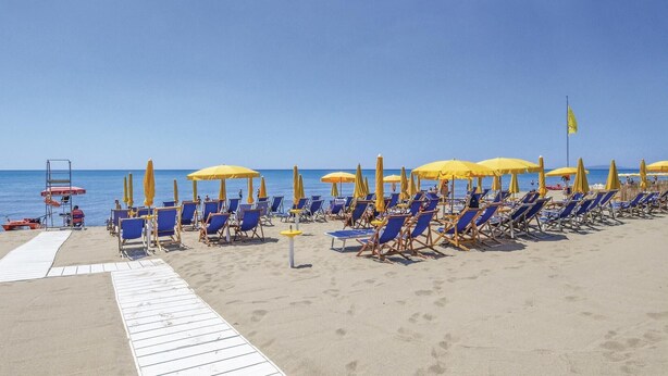 A beach with rows of blue lounge chairs and yellow umbrellas, a wooden walkway, and a lifeguard stand. - Stunning home in Castiglione d. Pescaia (Castiglione d. Pescaia)