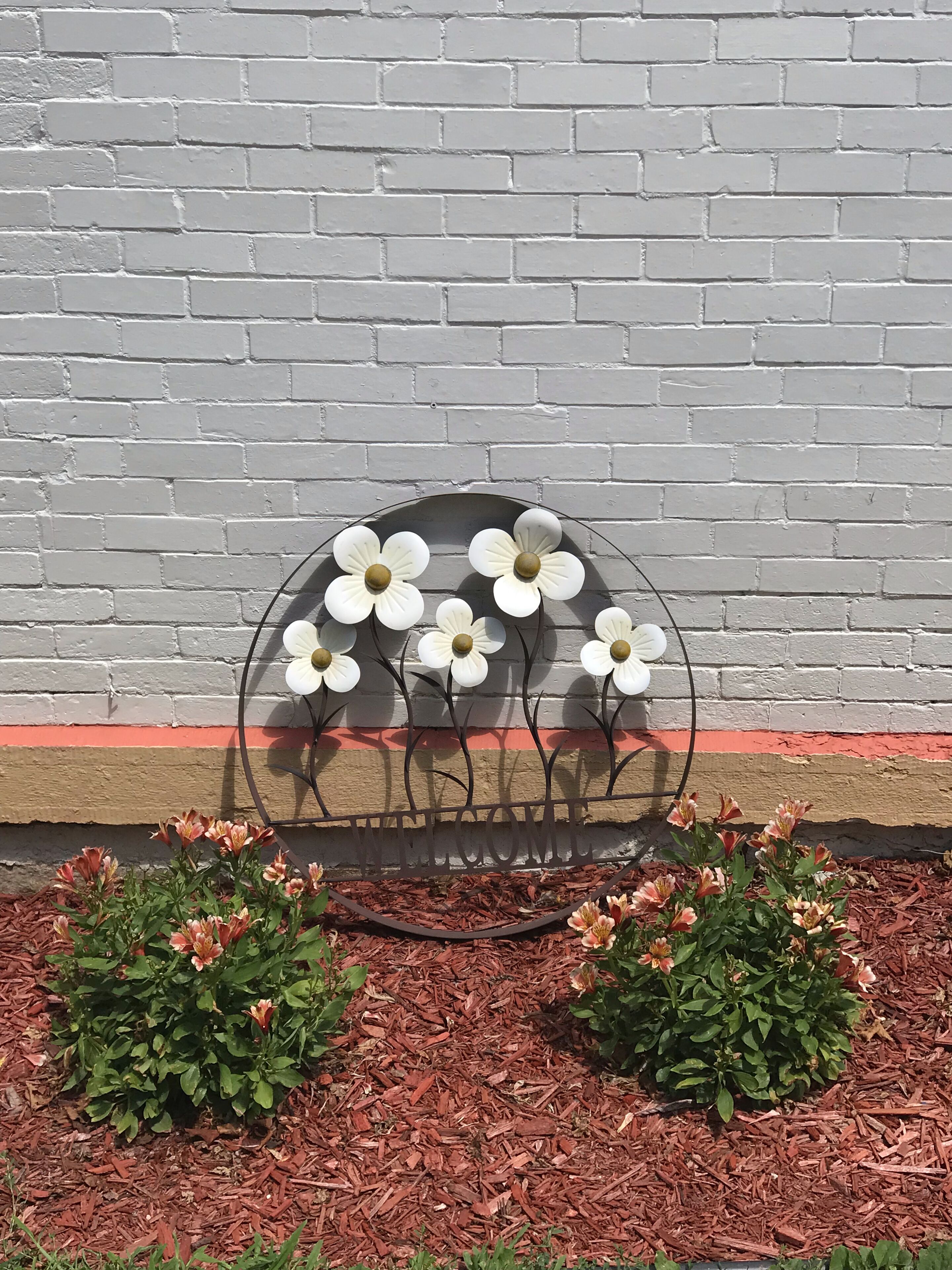 Une sculpture florale en métal, avec une pancarte indiquant « BIENVENUE », placée devant un mur de briques.