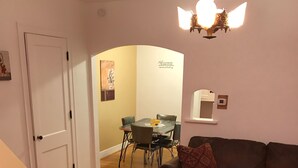 A living room with a brown sofa, a wooden coffee table, and a dining area with a table and chairs. - Historic Phelps Mansion;  main level Suite #1  (Decorah)