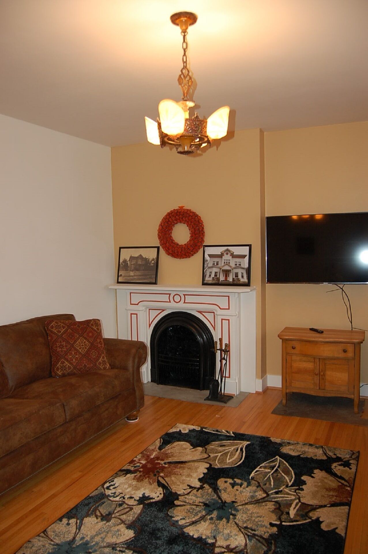 A living room with a fireplace, a brown sofa, a wooden cabinet, a television, and a patterned rug.