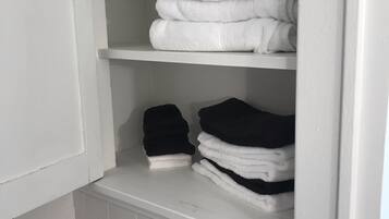 A white tiled bathroom with a white towel shelf containing neatly folded white and black towels.