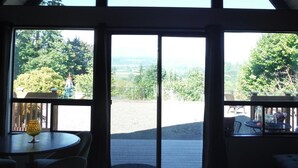A room with a large glass door leading to an outdoor deck, a table with chairs, and a view of the surrounding landscape. - Cascades View A Frame (Snohomish)