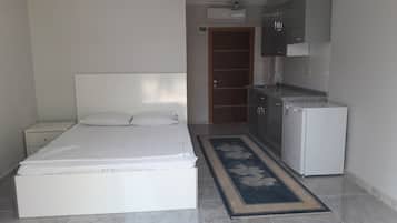 Una habitación pequeña y limpia con cama, mesita de noche, refrigerador y kitchenette.