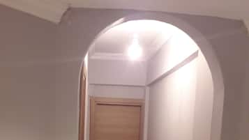 A narrow hallway with a wooden door at the end, tiled floor, and a ceiling light.