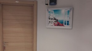 Ein Zimmer mit Holztür, Fliesenboden, einem an der Wand befestigten Projektor und einem gerahmten Bild.