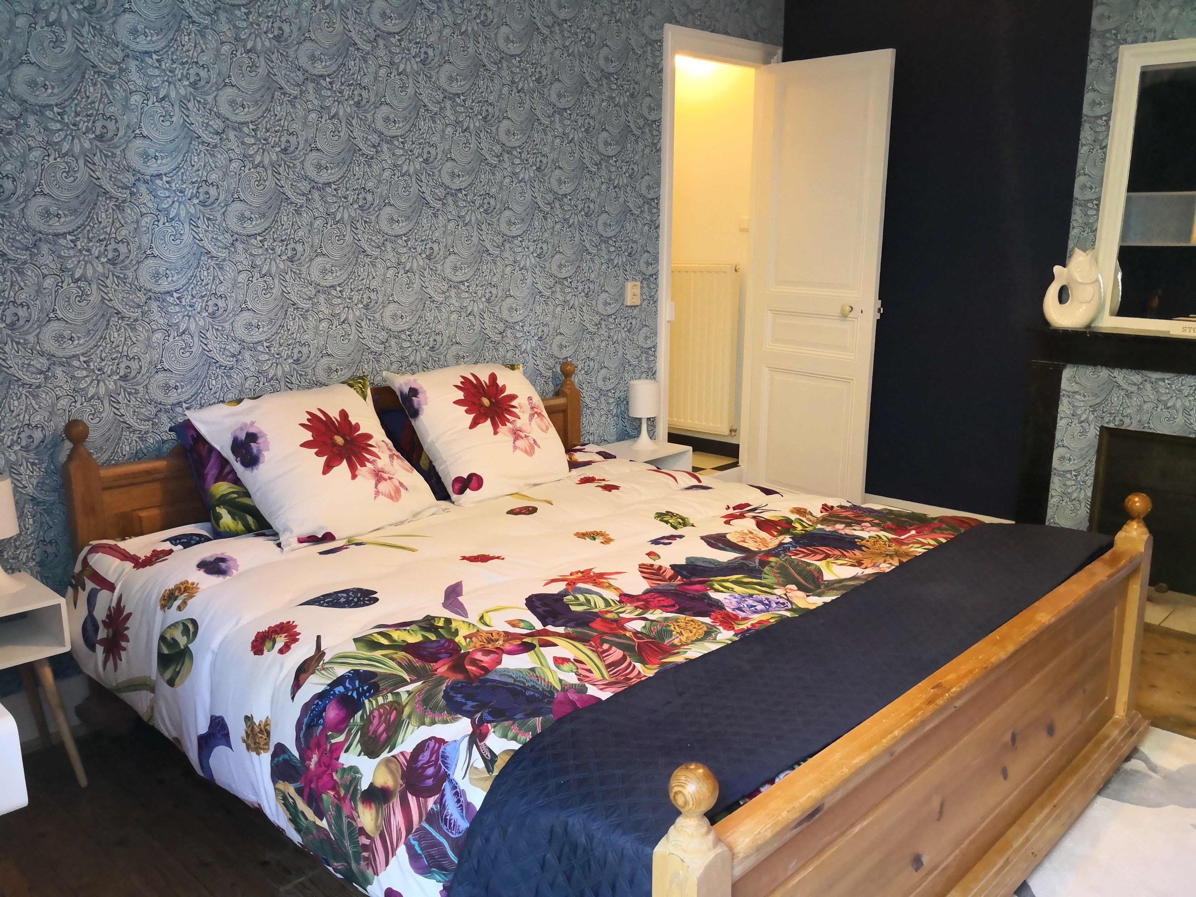 Ein Schlafzimmer mit einem blumigen Bettüberwurf, einem Holzkopfteil und einem Nachttisch mit Lampe.