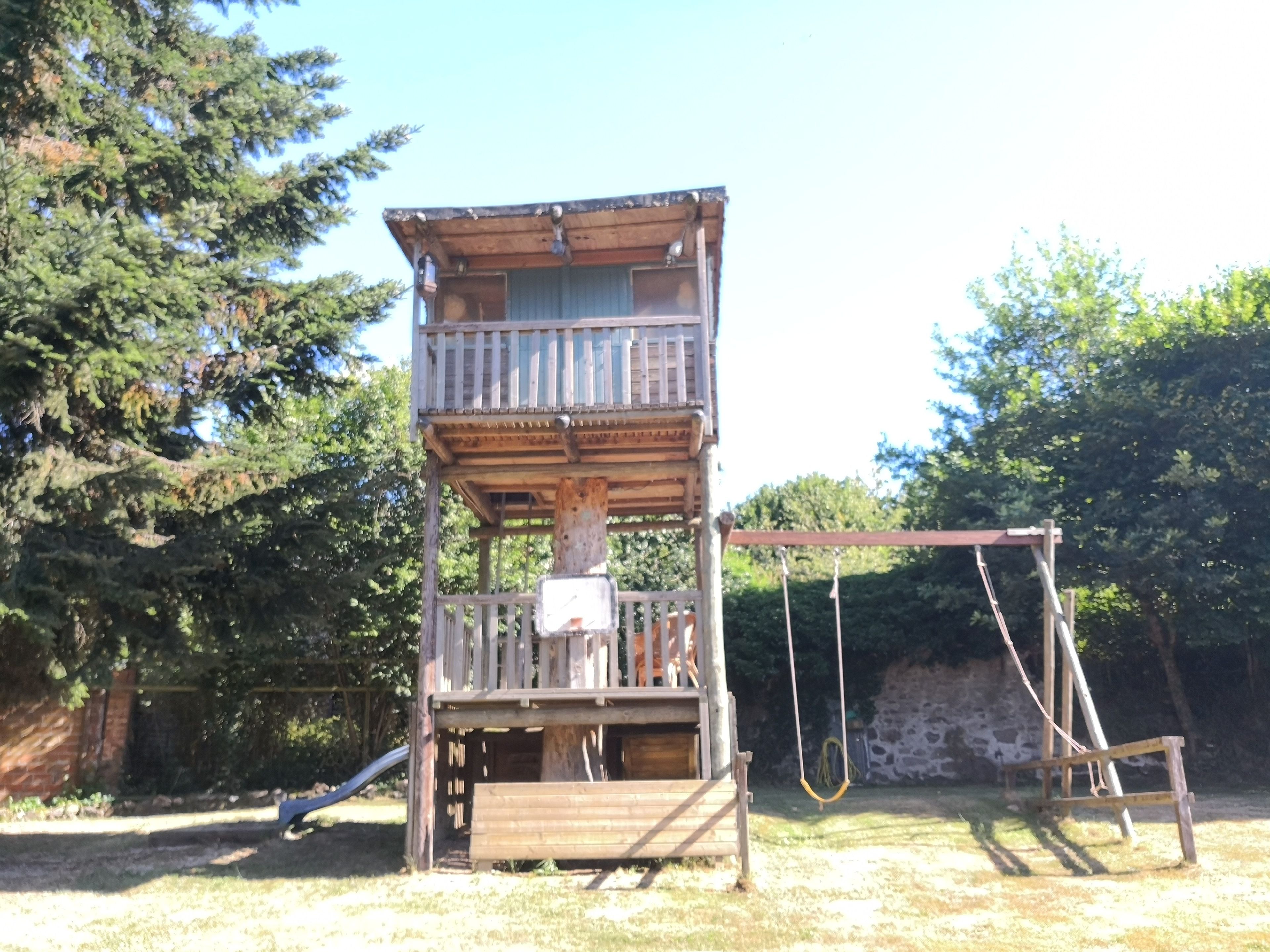 Una estructura de torre de madera con balcón, un columpio y un tobogán.
