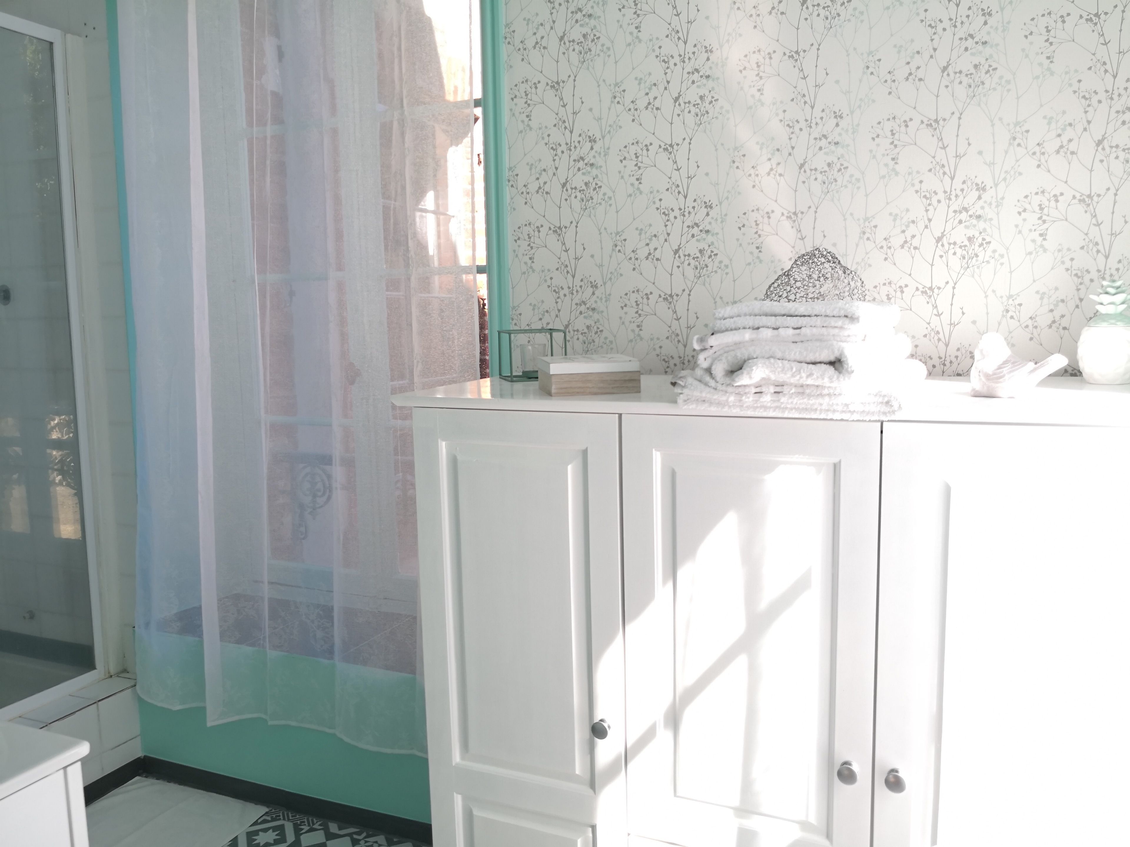 Un baño con tocador blanco, cabina de ducha con mampara de vidrio y papel tapiz con estampado floral.