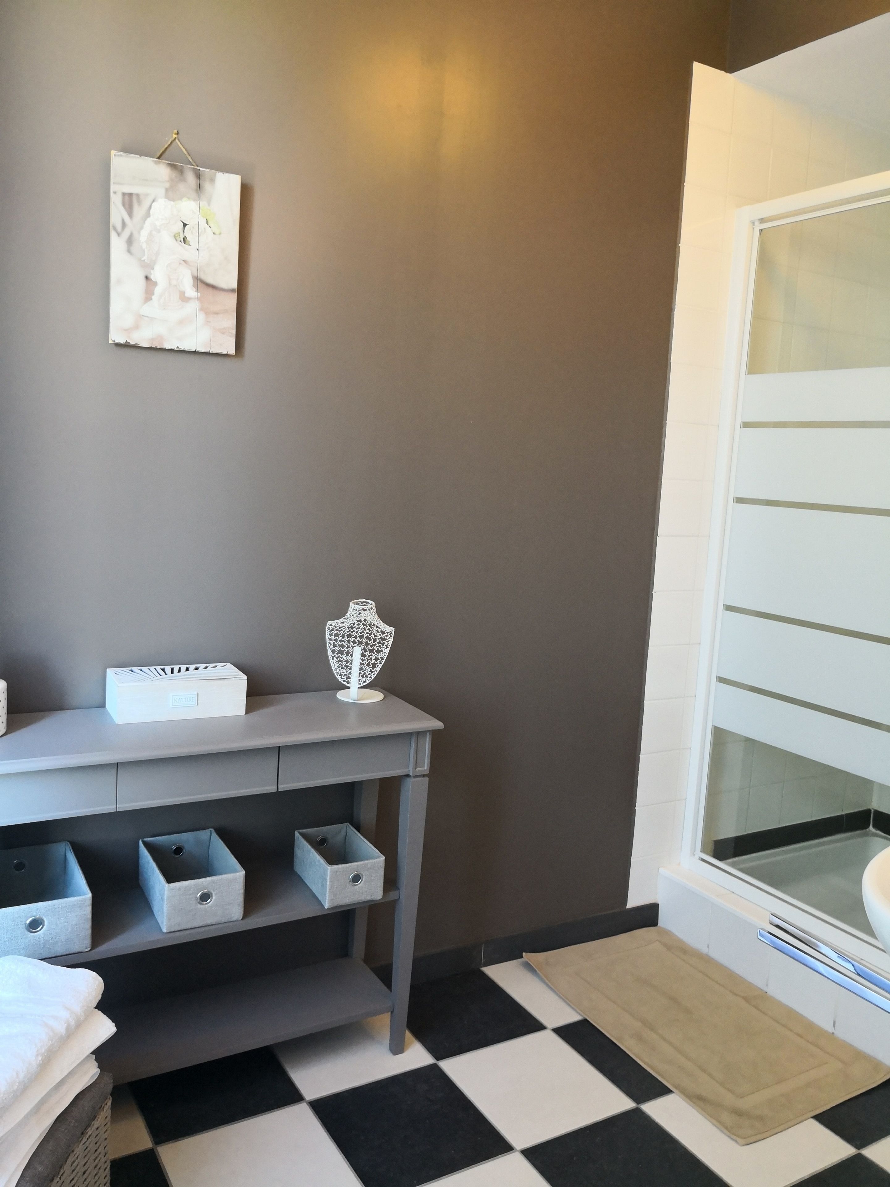 A bathroom with a checkered floor, a grey vanity with storage drawers, a white towel stack, and a framed picture on the wall.