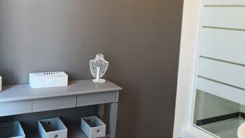 A bathroom with a checkered floor, a grey vanity with storage drawers, a white towel stack, and a framed picture on the wall.