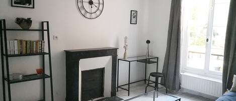 A living room with a fireplace, a bookshelf, a coffee table, and a window with curtains.