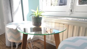 Una pequeña mesa de vidrio con una planta en maceta, dos sillas con cojines de estampado geométrico y un piso de madera.