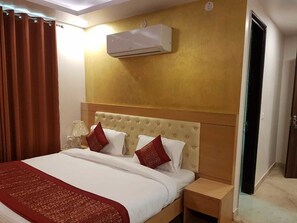 A hotel room with a bed, a nightstand, a lamp, and an air conditioning unit on the wall. - Mira International (New Delhi)