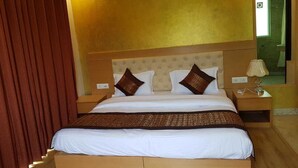 A hotel room with a large bed, a wooden headboard, a nightstand with a lamp, and a mirror on the wall. - Mira International (New Delhi)