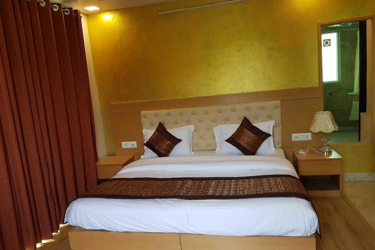 A hotel room with a large bed, a wooden headboard, a nightstand with a lamp, and a mirror on the wall.