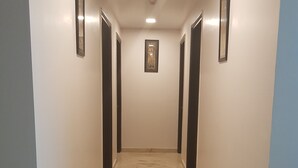 A hallway with a marble floor, framed pictures on the walls, and a ceiling light. - Mira International (New Delhi)