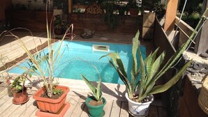 Un espace piscine agrémenté de plantes en pot et d’une terrasse en bois.