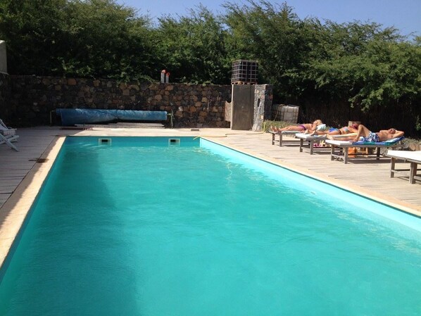 Una piscina rectangular con un muro de piedra y una zona cubierta al fondo.