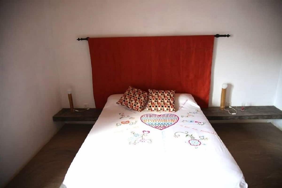 Een bed met een rode hoofdbord, twee gestreepte kussens en een bloemenbedekking.