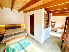 Un dormitorio con techo de madera, una cama con ropa de cama estampada, un ventanal pequeño y un armario de madera.