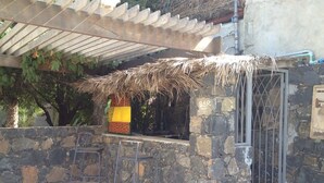 Un espace bar extérieur avec des murs en pierre et un toit de chaume, deux tabourets de bar en métal et un mur en pierre.