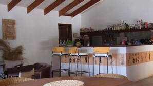 Un coin repas rustique avec une table en bois, des tabourets de bar et un comptoir doté d’étagères remplies de bouteilles.