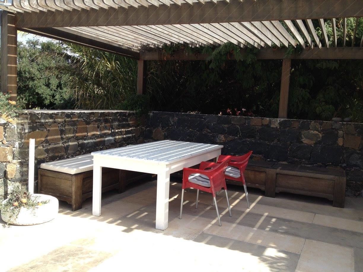 Een terras buiten met een tafel en stoelen, stenen muren en een pergola.