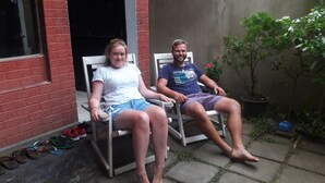 Two people sitting on outdoor chairs in a garden area with a brick wall and potted plants. - Villa Vidura (Galle)
