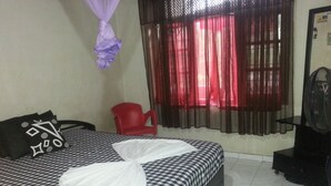 A hotel room with a checkered bedspread, a red chair, a black fan, and a window with red curtains. - Villa Vidura (Galle)
