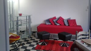 Una habitación compacta con un sofá rojo, dos otomanes negros, una mesa de vidrio, una silla y un suelo a cuadros.