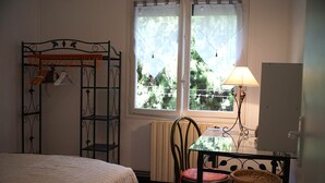 Una habitación con cama, una mesa con lámpara, una silla y una ventana con vista a árboles.