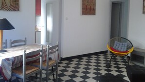 Una habitación con piso a cuadros, una mesa de comedor con sillas, una lámpara y un sillón con cojín.