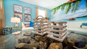 Une structure en bois posée sur une table en verre, un mur bleu orné de tableaux encadrés, un canapé blanc et une lampe.