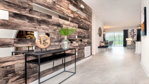 A modern living room with a wooden wall feature, a console table with a vase, and a dining area in the background.
