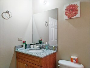 A bathroom with a granite countertop sink, wooden cabinets, a large mirror, and a toilet. - The Sojourn at the Vistas (Runaway Bay)