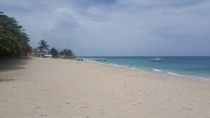 A wide sandy beach with a few boats in the water, palm trees, and a clear sky. - The Sojourn at the Vistas (Runaway Bay)