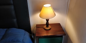 A bedside table with a lamp, a green drawer, and a blue bedspread.