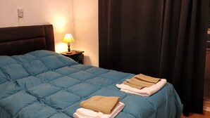 A bed with a blue quilt, a nightstand with a lamp, and folded towels on the bed. - Cute Abasto Apartment (Buenos Aires)